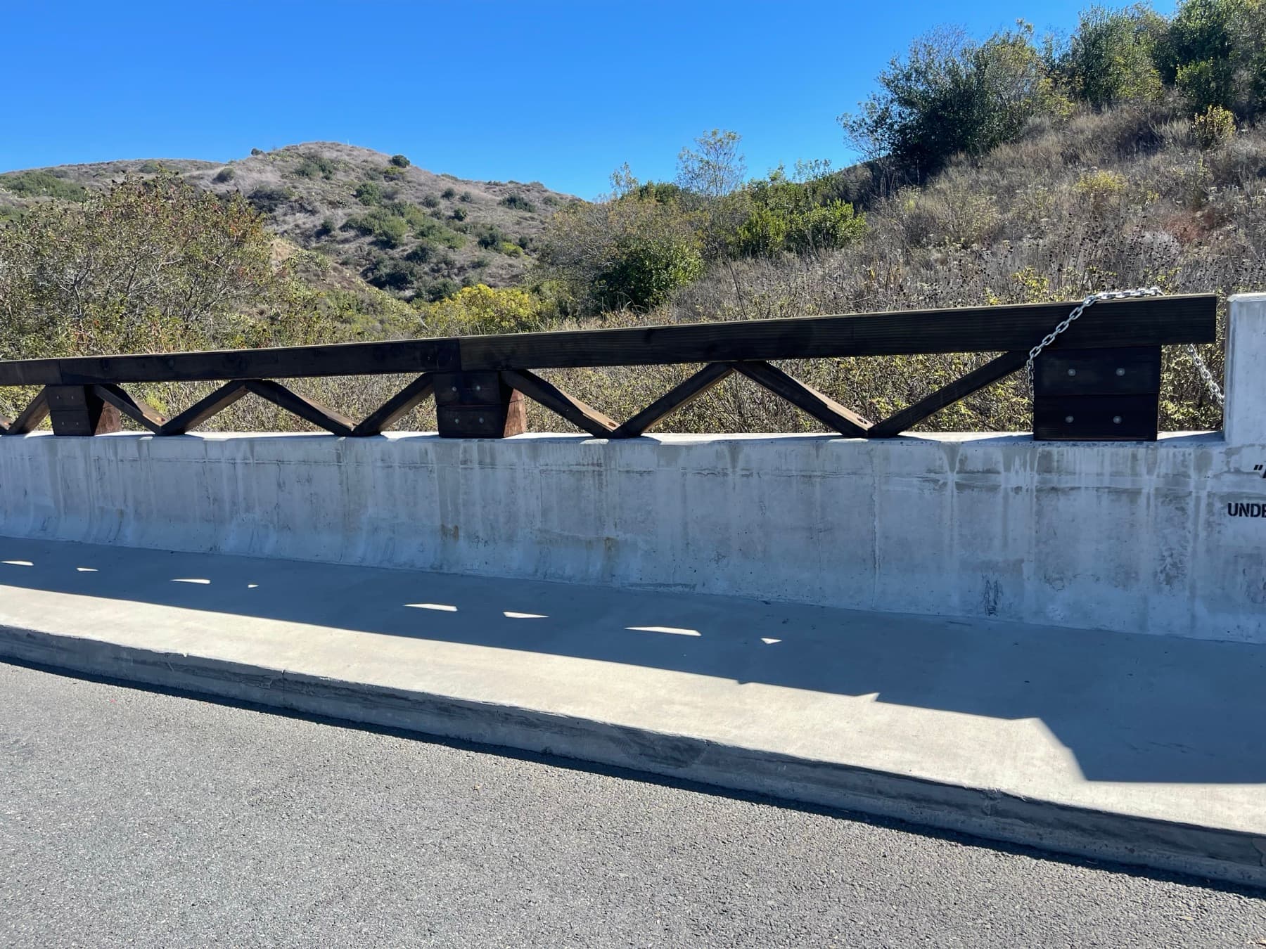 Timber guardrail detail along a bridge edge in a hillside setting